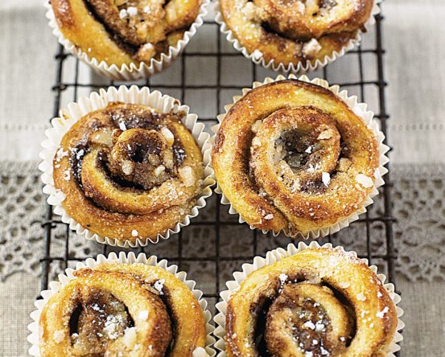 Six cinnamon whirls shown dusted with icing sugar on a wire rack