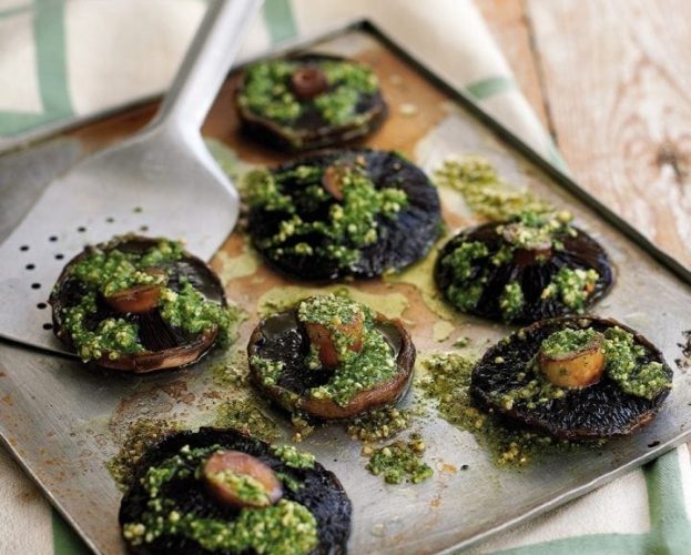 Mushrooms stuffed with green rocket pesto, shown on a baking tray