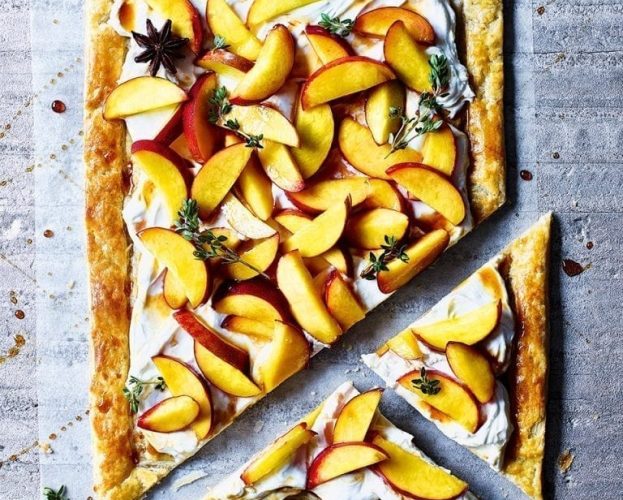 Peach tart made with rough puff pastry shown on a grey background