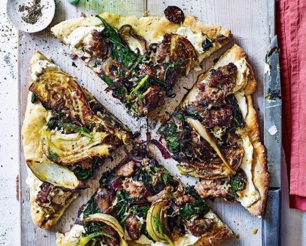 Griddle pan pizza topped with sausage and fennel shown on a grey board