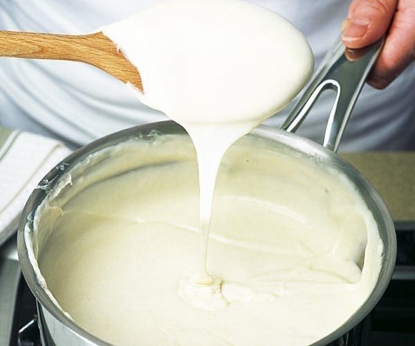 White sauce, bechamel sauce, shown dripping off a spoon into a pan