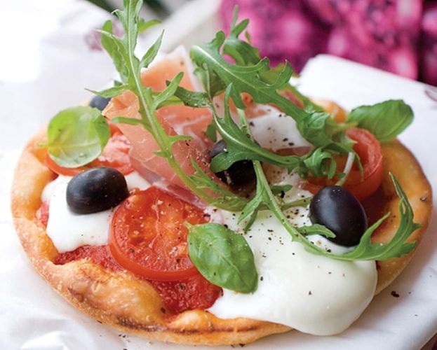 A pizza with mascarpone cheese, rocket and black olives on top