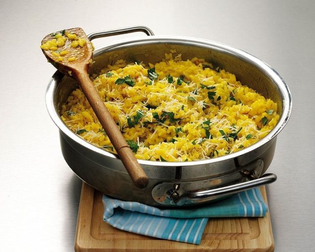 Bright yellow risotto alla Milanese shown cooked in a silver pan