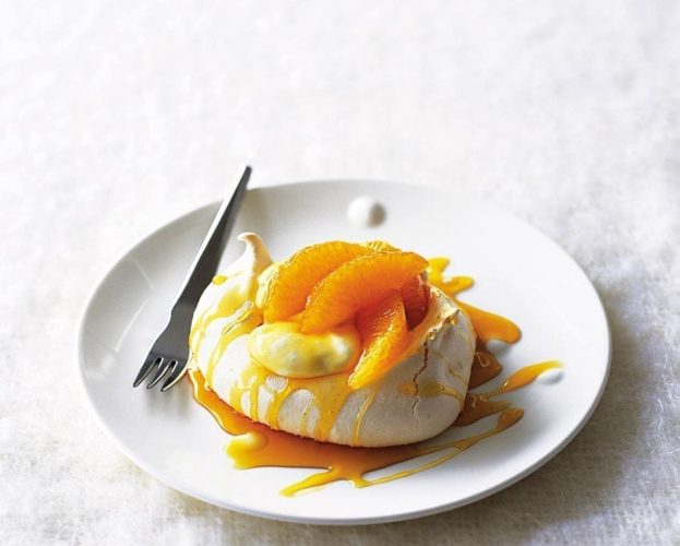 A single pavlova with orange and caramel on top, sitting on a white plate