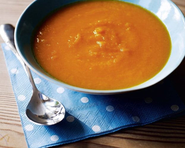 A bowl of carrot and orange soup in a blue bowl, with a spoon by the side