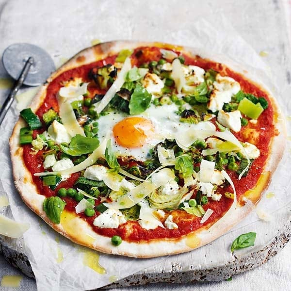 Pizza topped with a cooked egg and green veg