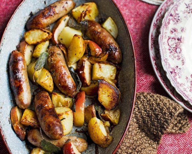 Sausages, apples and potatoes shown cooked in a casserole dish