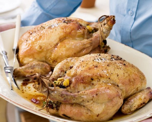 Two roast chickens shown on a white plate being carried by a person
