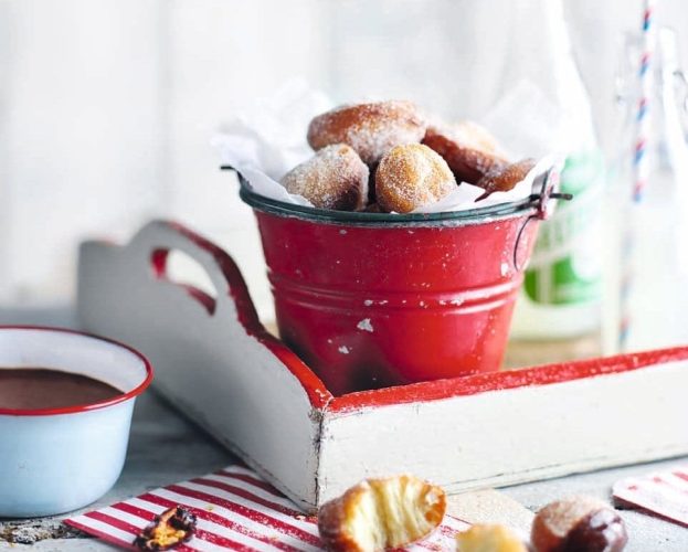 Sugar-dusted cinnamon beignets shown in a little red bucket
