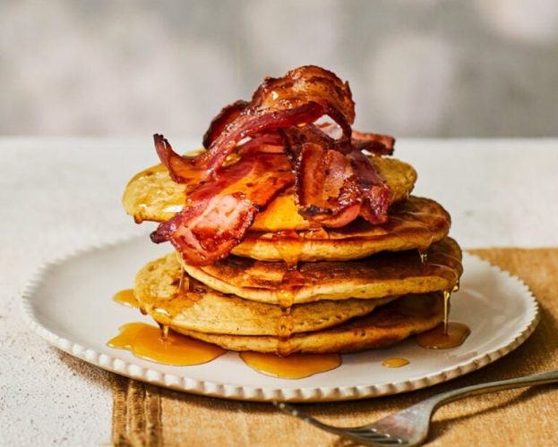 A stack of pancakes topped with crispy bacon and maple syrup