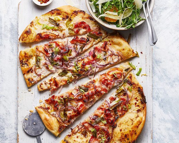 A pizza shown sliced diagonally on a wooden board
