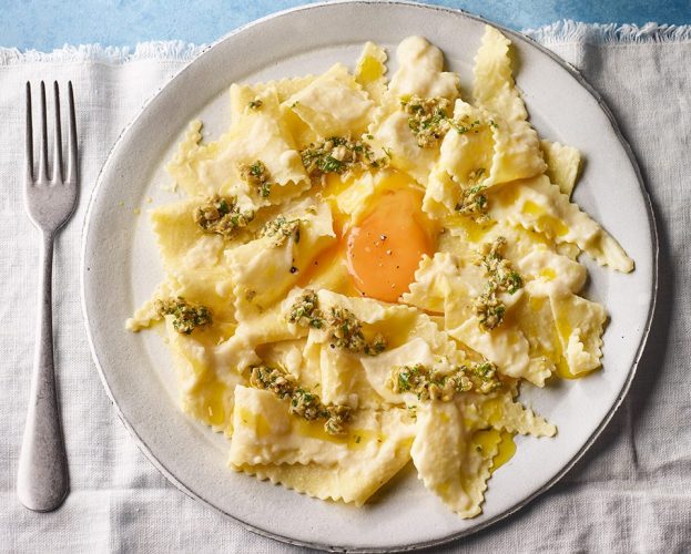 An open-style lasagne shown cooked on a plate, with an egg yolk at the centre