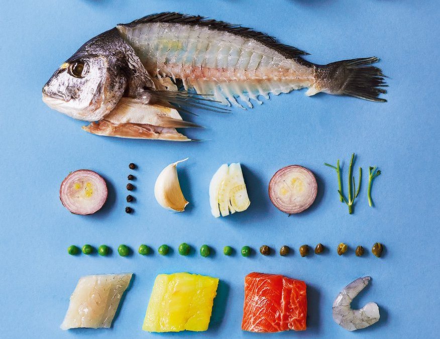 The ingredients of a fish pie laid out together, including a whole filleted fish, spinach, potatoes, prawns and soft herbs