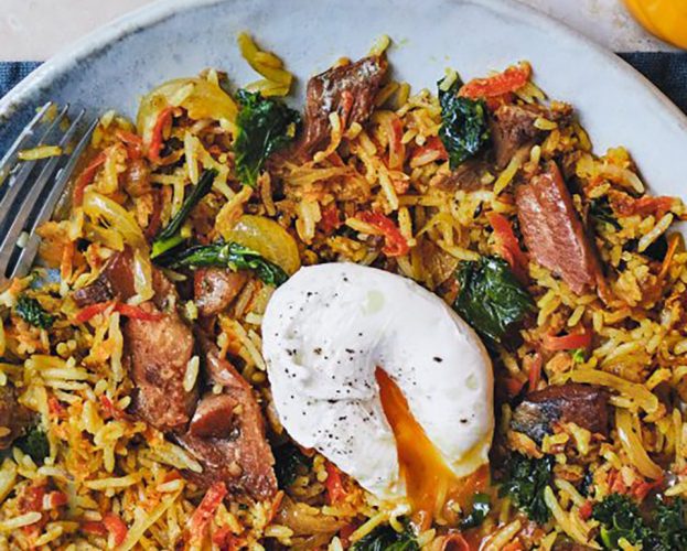 A close up of a bowl of fried rice, with shreds of carrot, kale and kipper, and a poached egg on top