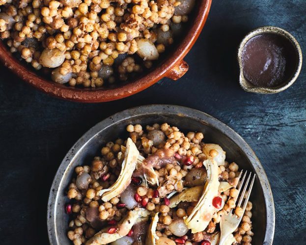 A bowl of Lebanese stew moghrabieh, topped with chicken and pomegranate seeds