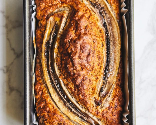 A banana bread in its tin, topped with two banana halves