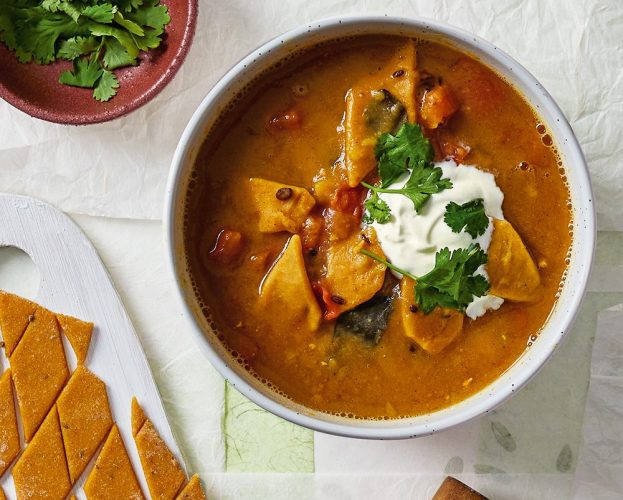 A bowl of dal dhokli with extra uncooked dumplings on the side, with a bowl of coriander