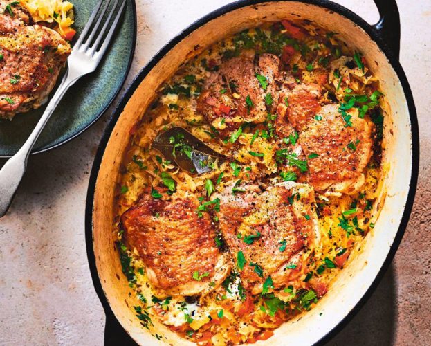 A casserole dish filled with choucroute garni and golden chicken pieces, topped with chopped parsley