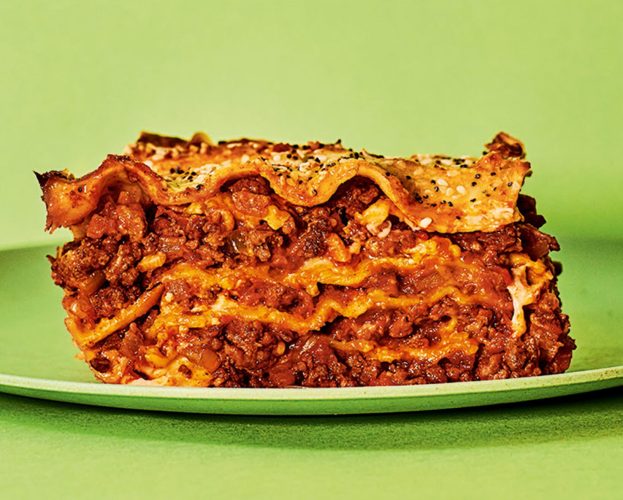 A slice of layered lasagne on a green background