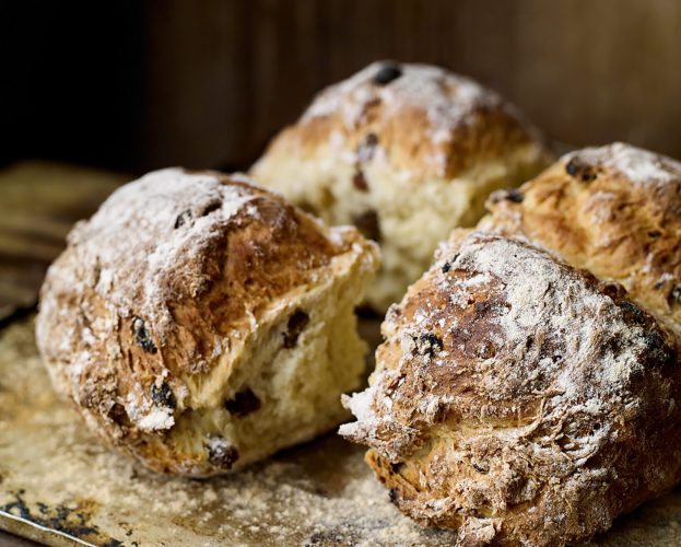A loaf of spotted dog (enriched soda bread made with sugar, sultanas and egg), scored into four pieces, with one pulled out