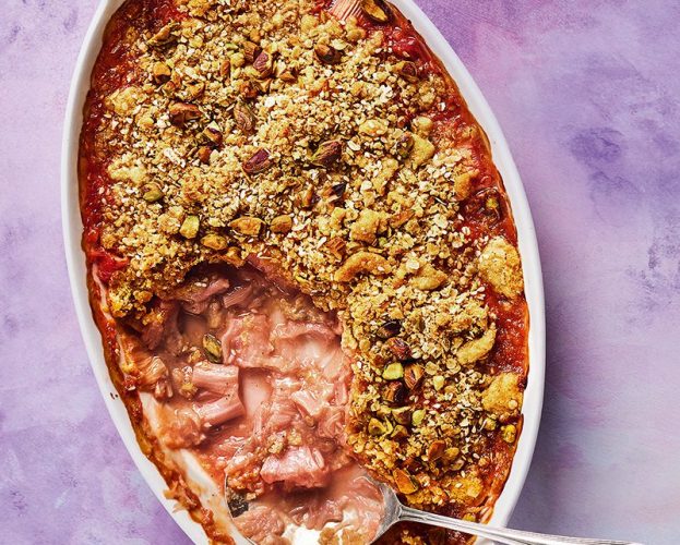 An overhead view of a dish of golden rhubarb and rose crumble, with some spooned out