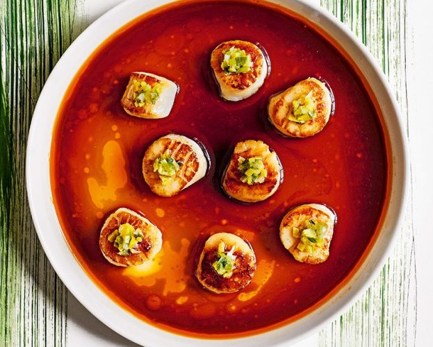 An overhead view of scallops in a chilli-soy dressing on a background painted with green spring onions