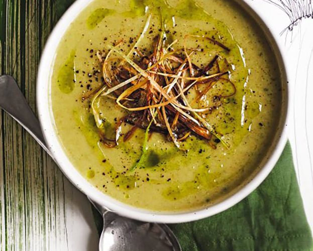 An overhead view of a bowl of spring onion soup topped with fried spring onions