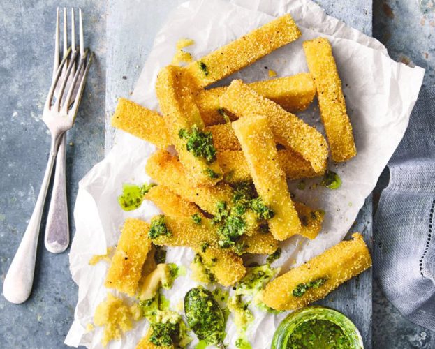 A pile of polenta chips on a board, drizzled with salsa verde