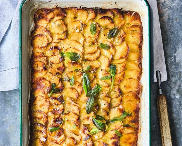 A tray of golden brown pommes anna, thinly sliced potatoes, topped with sage leaves