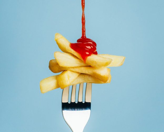 A fork spearing chips, with ketchup drizzling