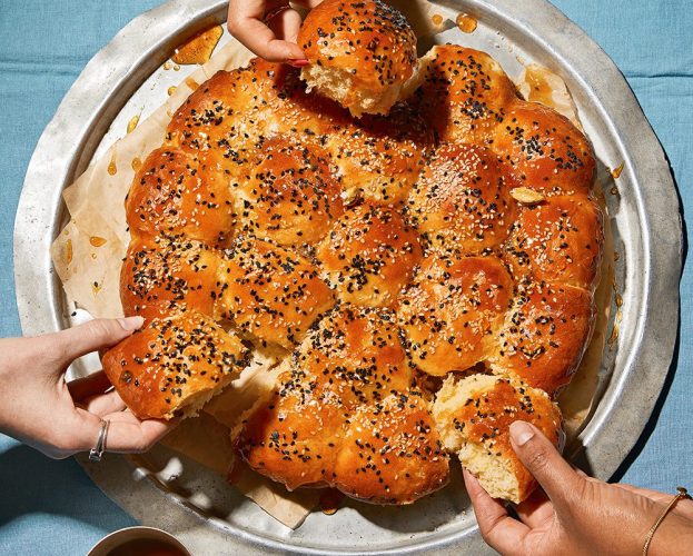 Overhead view of khaliat nahal (Omani honeycomb bread), with threee hands reaching in to tear off pieces of bread