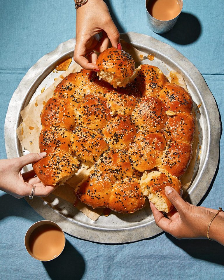 Overhead view of khaliat nahal (Omani honeycomb bread), with threee hands reaching in to tear off pieces of bread