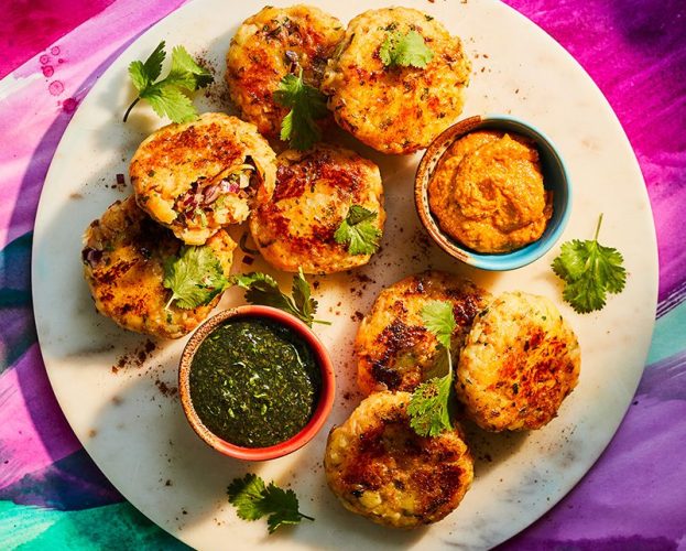 An overhead view of a plate of aloo tikki (potato patties), sprinkled with coriander and with two dips on the side