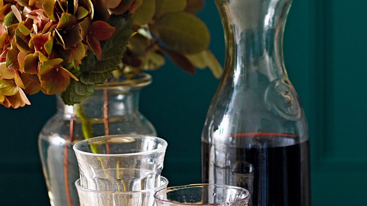 A carafe of red wine with a filled glass in the foregound