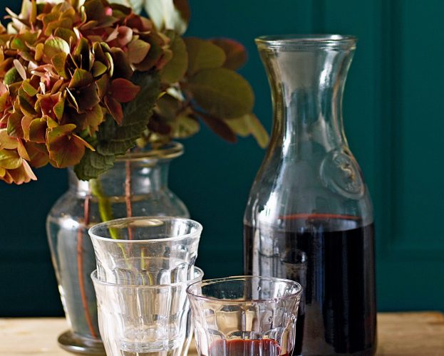 A carafe of red wine with a filled glass in the foregound