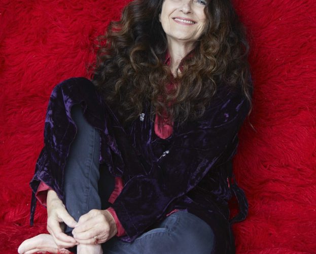 A smiling woman with brown hair sits casually on a red sofa; Ruth Reichl interview