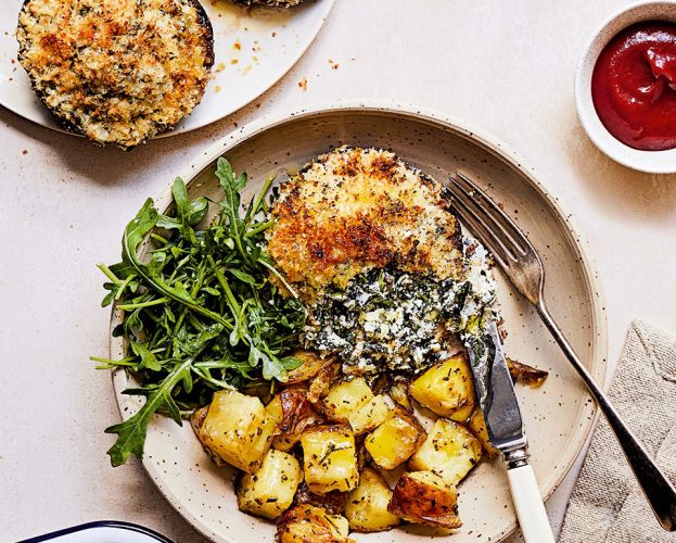 Spinach and ricotta stuffed mushrooms on a plate with with rosemary potatoes and rocket and a pot of tomato ketchup on the side