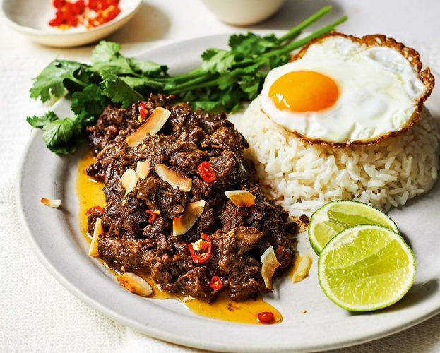 A portion of caramelised coconut beef, served with rice, coriander, a fried egg and lime wedges