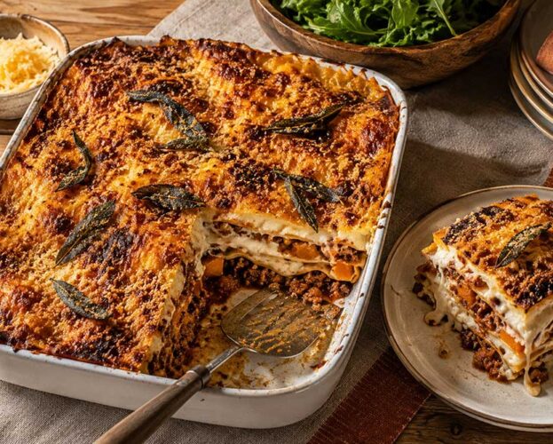 Sausage, squash and sage lasagne in a large dish with one portion lifted out to show the golden layers