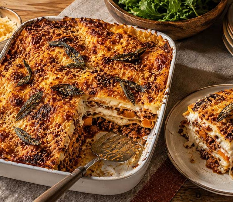 Sausage, squash and sage lasagne in a large dish with one portion lifted out to show the golden layers