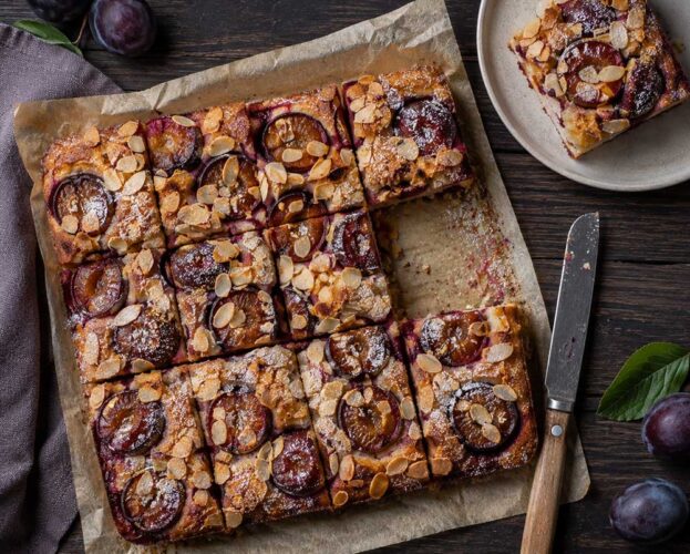 Damson and almond traybake cut into squares, with halved damsons and flaked almonds on top
