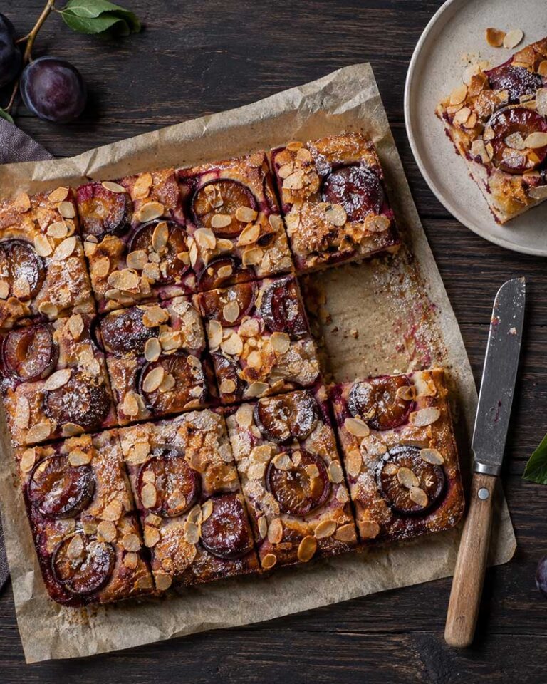 Damson and almond traybake cut into squares, with halved damsons and flaked almonds on top