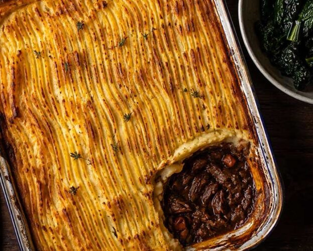 Venison cottage pie with golden celeriac mash in a large dish, one portion removed to show the rich mushroom filling