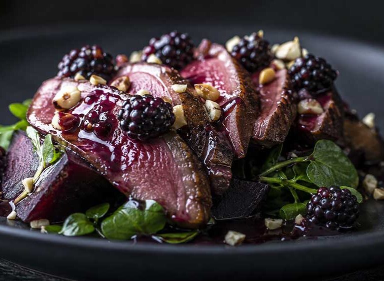 Sliced pink pigeon breast on roast beetroot and watercress with a blackberry sauce and toasted cobnuts