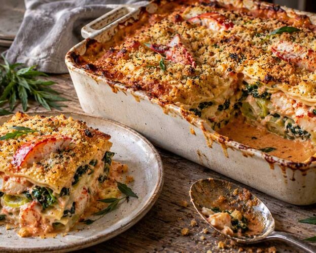 Lobster, leek and spinach lasagne with a golden crumb, one portion served on a plate beside the dish