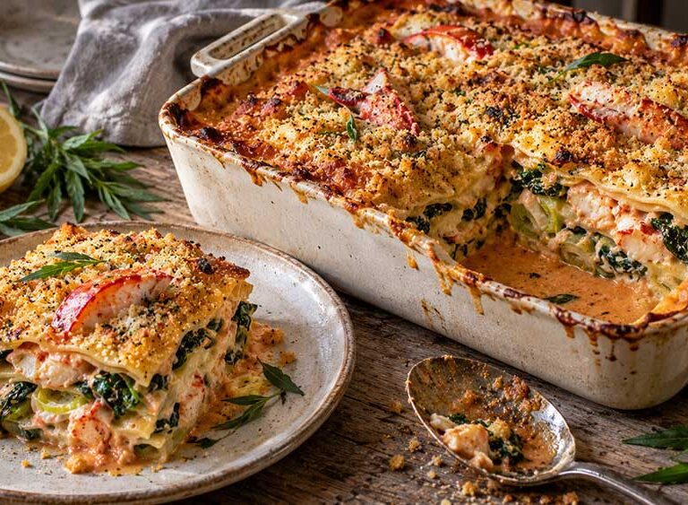 Lobster, leek and spinach lasagne with a golden crumb, one portion served on a plate beside the dish
