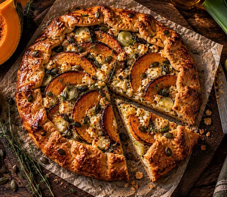Rustic pumpkin, leek and Lancashire cheese galette on a board with one wedge cut