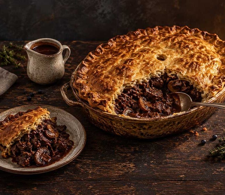 Venison, red wine and mushroom pie with a golden suet crust, one portion served to show the dark, glossy filling