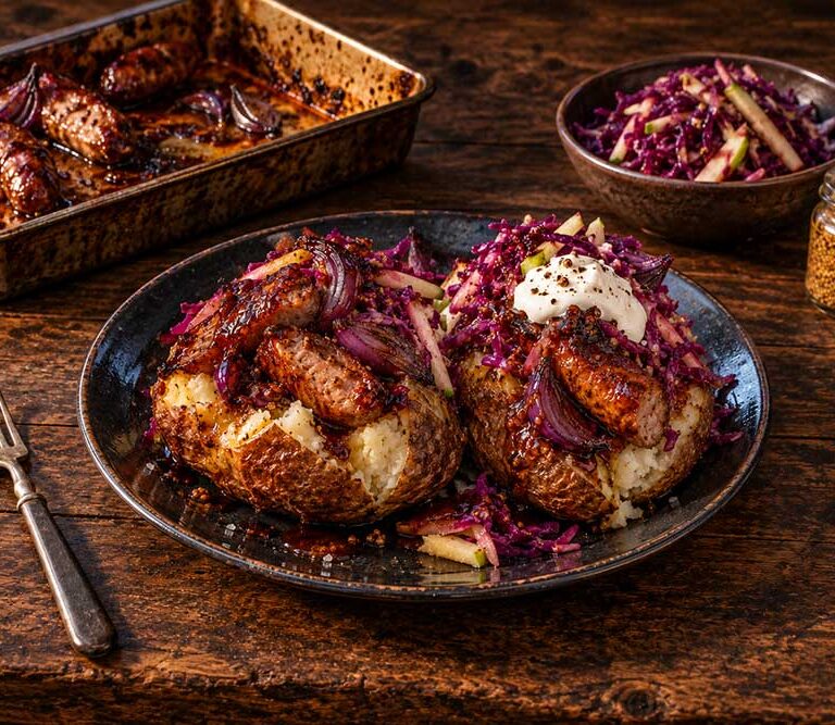 Sticky sausage jacket potatoes topped with glazed sausages, roast red onion, soured cream and red cabbage slaw