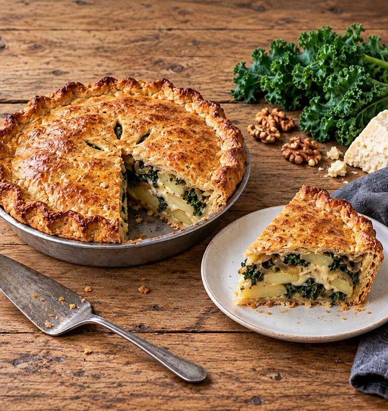 Cheese, onion and kale pie with golden walnut pastry, one wedge cut to show the potato, cheese and kale filling